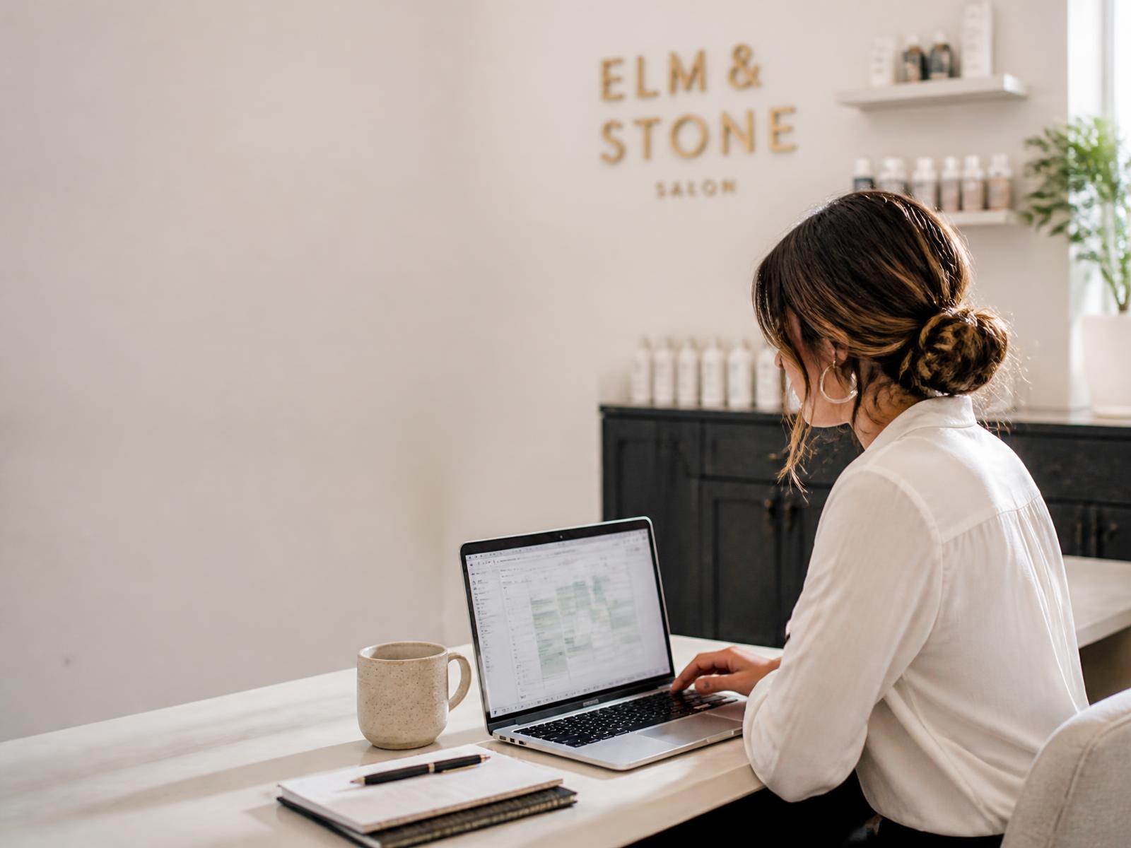 Salon owner at a laptop in the back office running her entire business on NeonO
